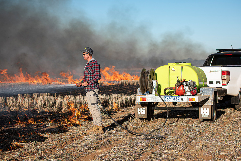 A man is using a fire patrol trailer to extinguish a fire in the rice field.